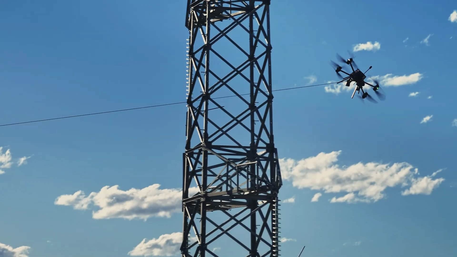 A Callisto pulling a pilot line past a steel transmission tower against a blue sky
