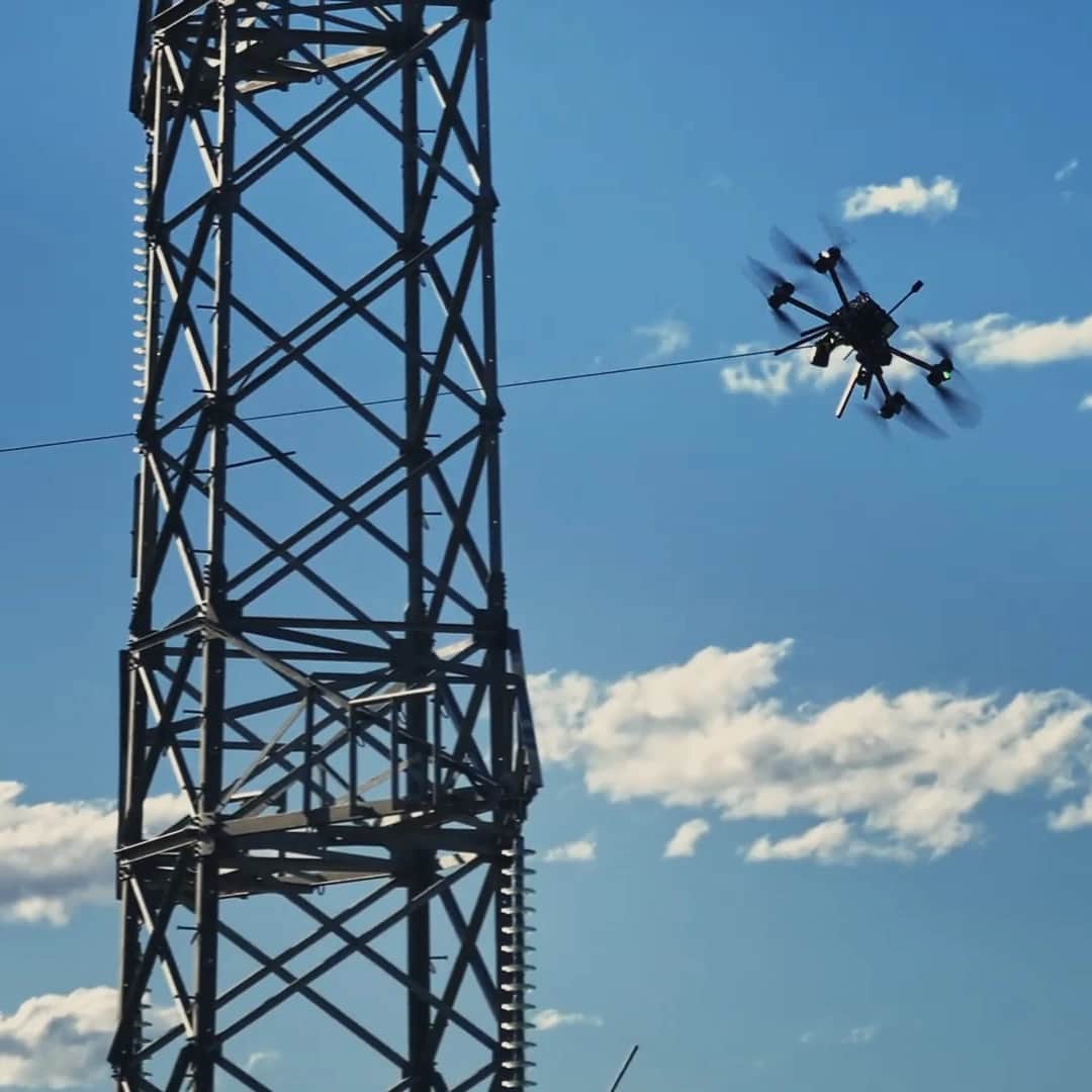 A Callisto pulling a pilot line past a steel transmission tower against a blue sky