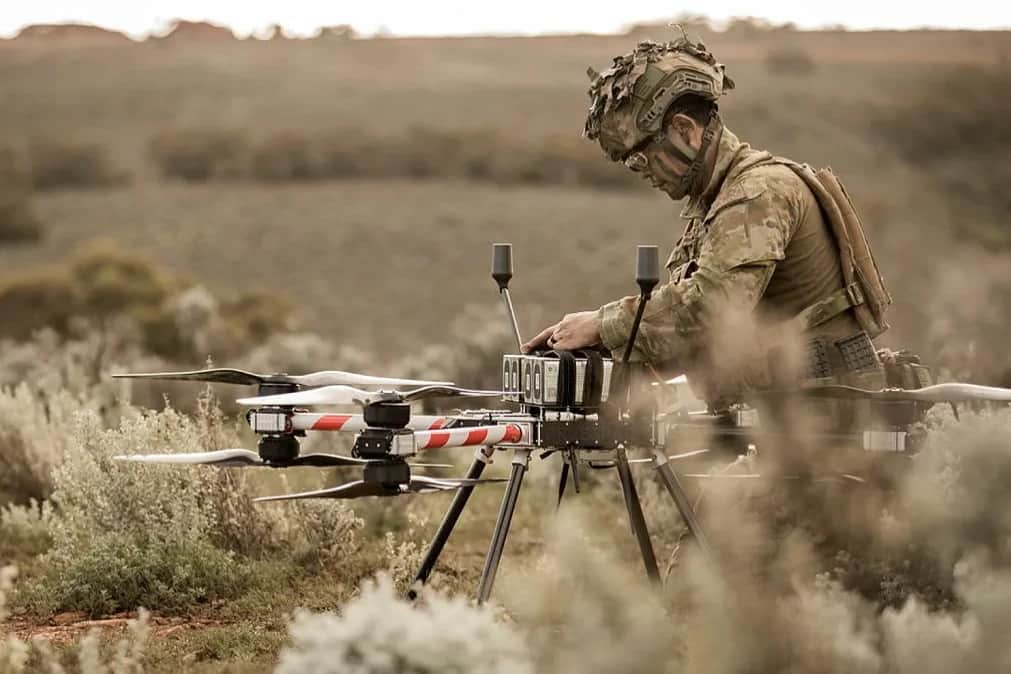 An Australian Army soldier bending over a Callisto on the ground in low scrub