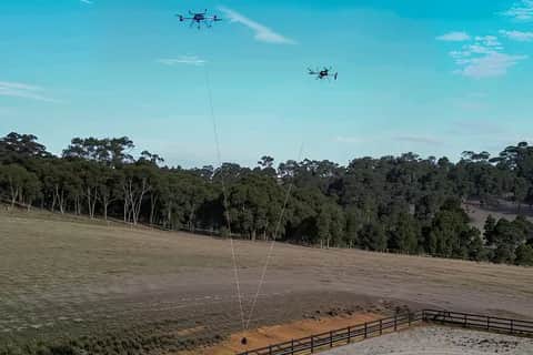Two Callisto aircraft in the air above a paddock, each on a line to one shared load
