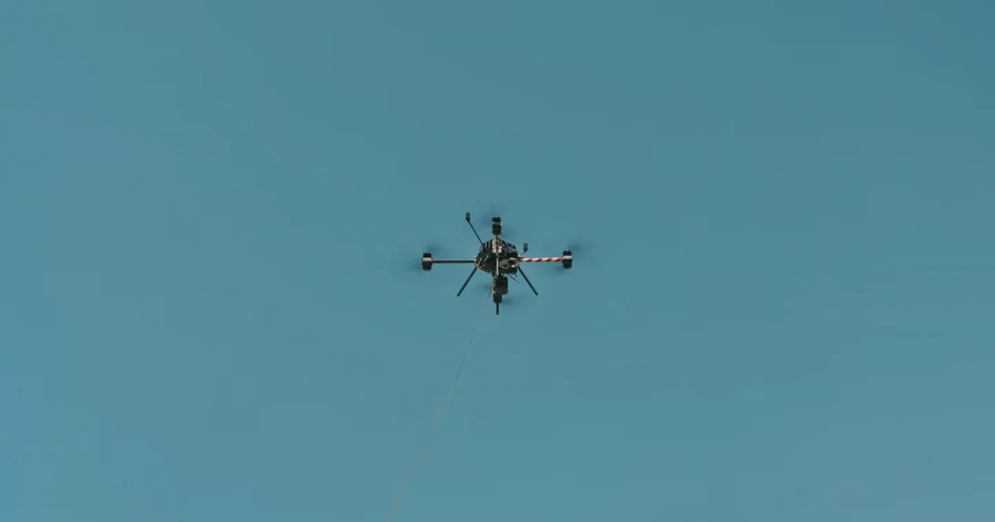 A Callisto stringing line against a clear sky, then beside a pole and an insulator string