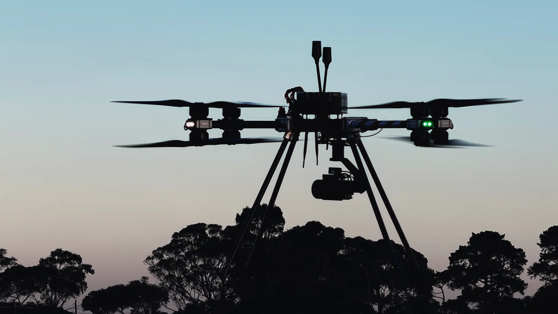 A Callisto 50 with its gimbal camera hovering against a dusk sky above a treeline