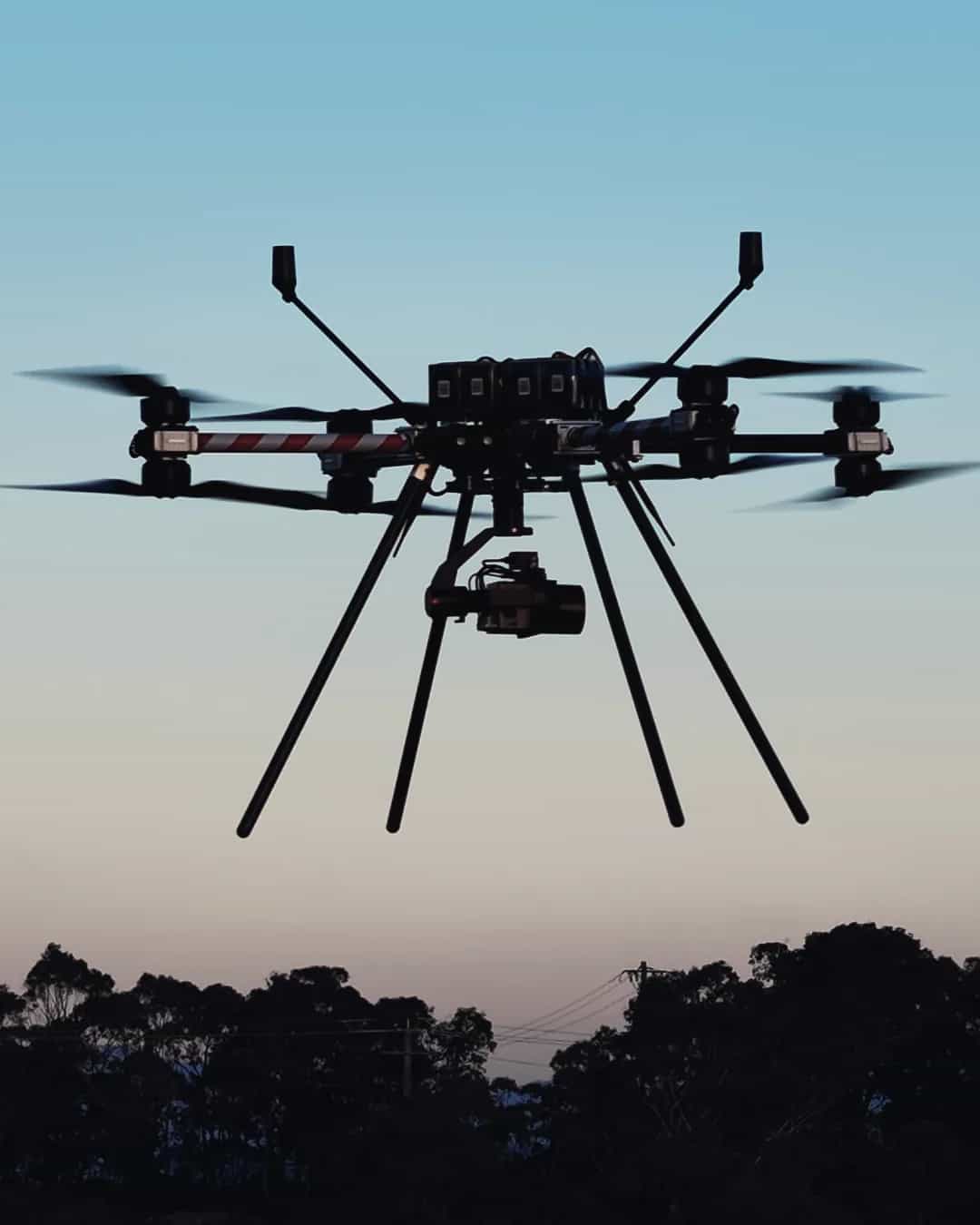 A Callisto 50 with its gimbal camera hovering against a dusk sky above a treeline