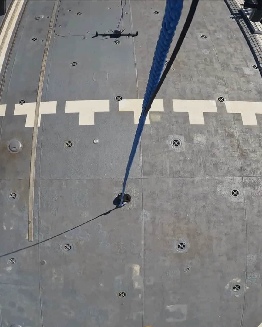 Looking down from a Callisto at a naval vessel's flight deck, its tether running to the deck