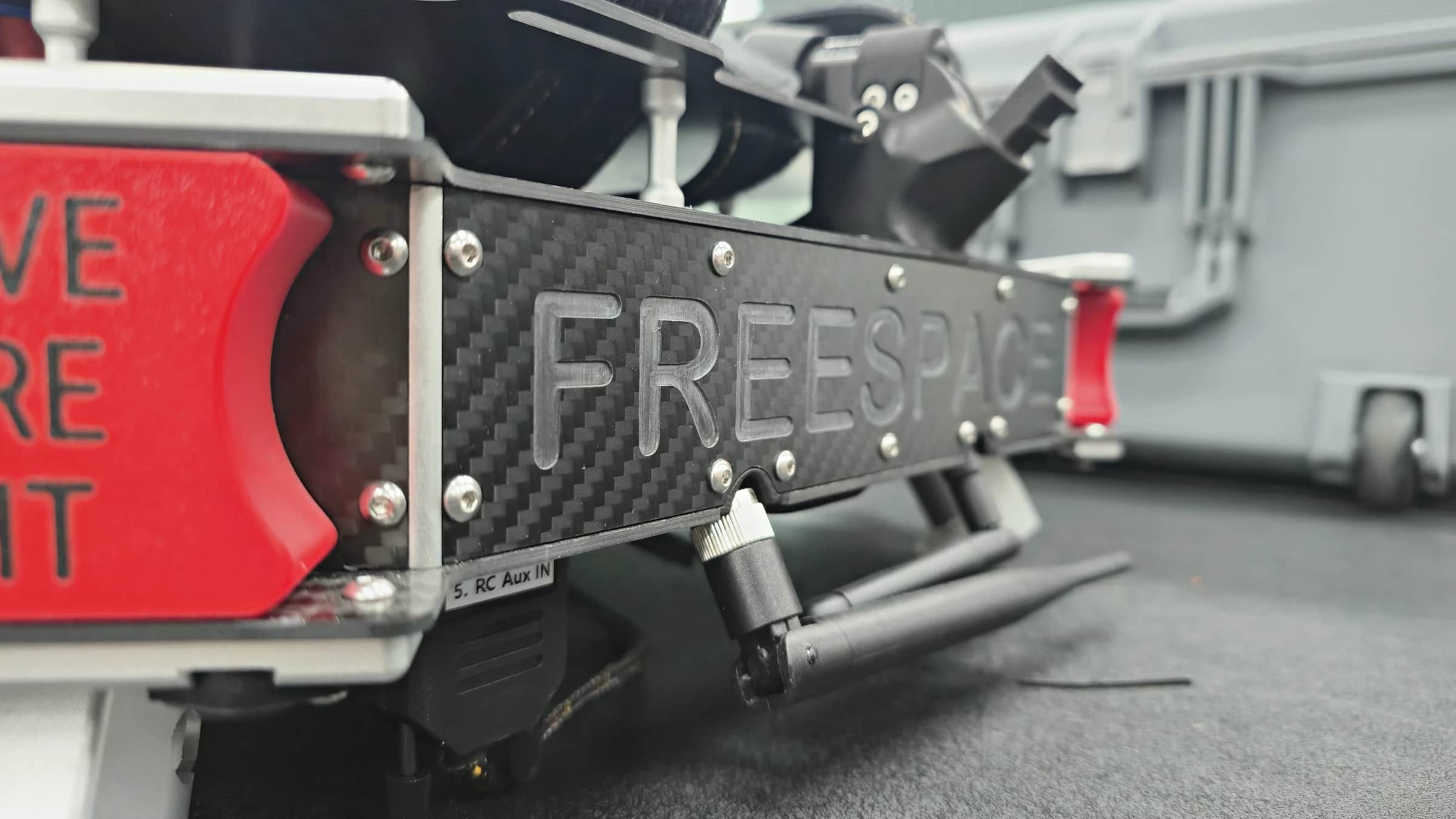The Callisto's carbon fibre body plate embossed FREESPACE, its connectors and the red remove before flight cover beside it