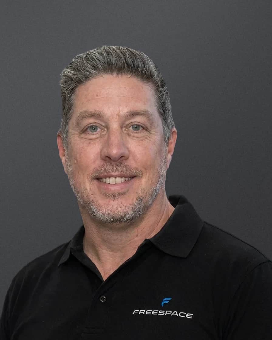 Richard Hall, head and shoulders, smiling, in a black Freespace polo against a soft grey studio backdrop