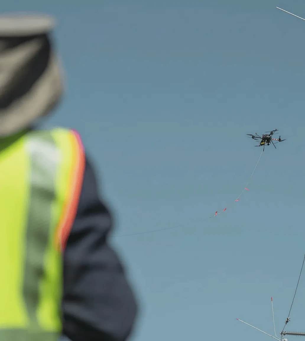 A line worker in high-visibility clothing watching a Callisto pull a pilot line across the sky